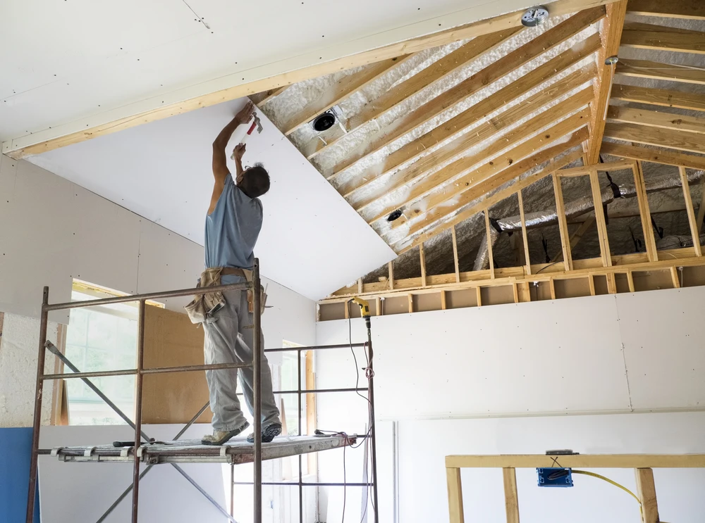 Ouvrier sur échafaudage installant une plaque de plâtre au plafond dans une maison en construction