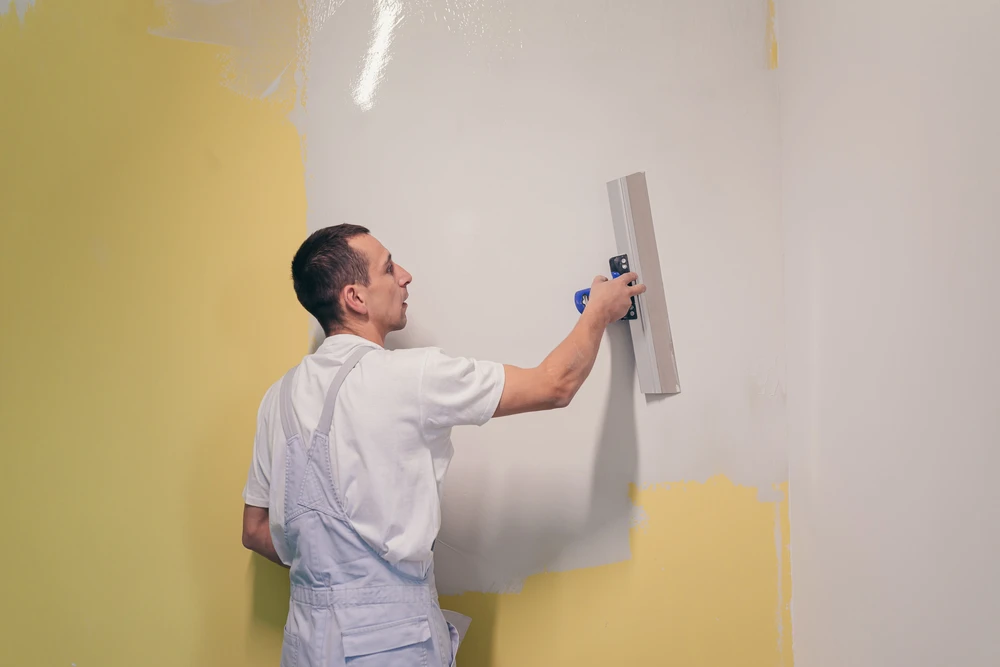 Un ouvrier applique putty aux murs de l'appartement avec une spatule, fait des réparations dans une nouvelle maison