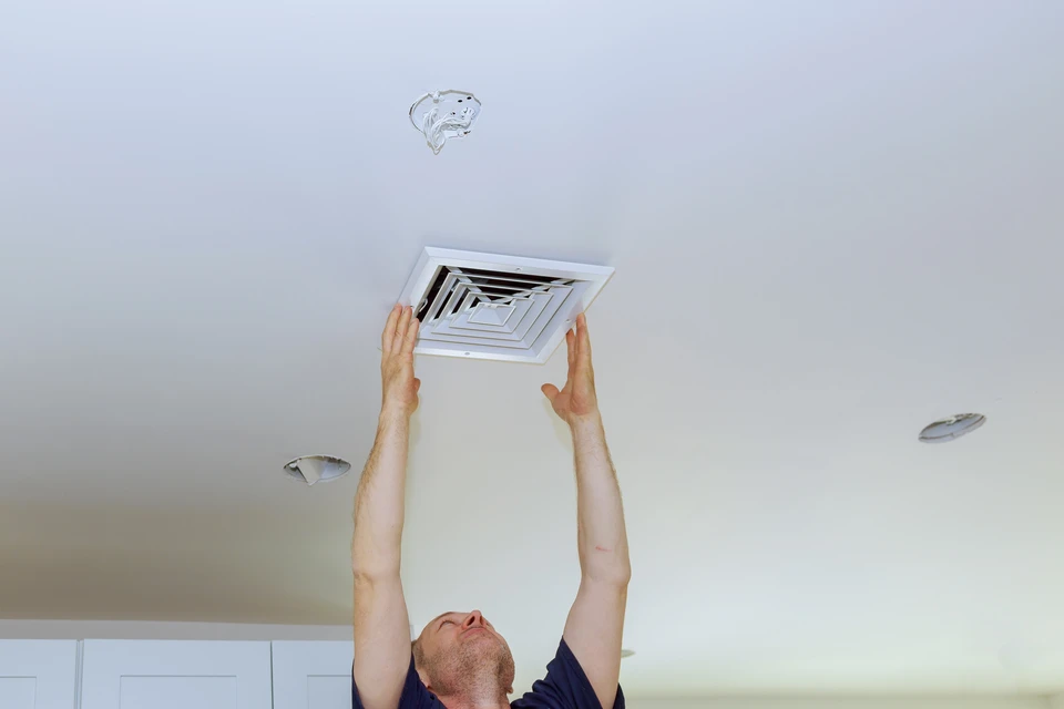 Homme installant ou retirant une grille de ventilation carrée au plafond d'un intérieur résidentiel