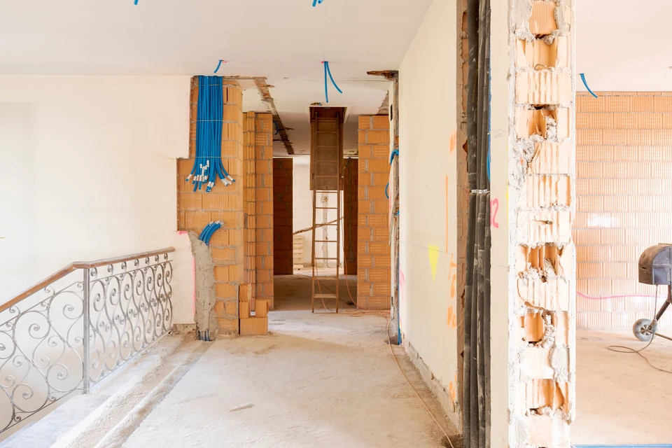 Chantier de rénovation intérieure avec murs en briques creuses apparentes, câbles électriques bleus en attente, escalier avec rampe en fer forgé décorative
