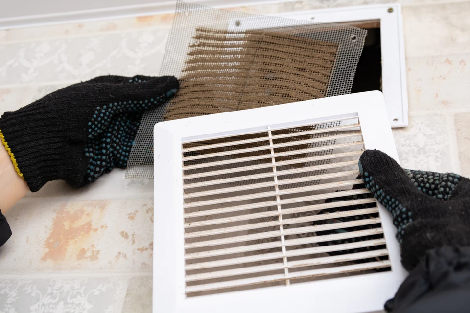 Intérieur résidentiel, mains gantées retirant grille de ventilation murale blanche