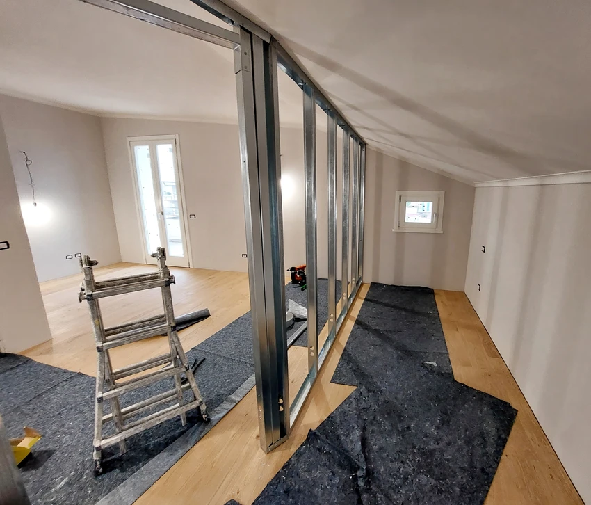 Un professionnel en vêtements de travail beige et blanc installe un faux plafond suspendu dans un intérieur résidentiel