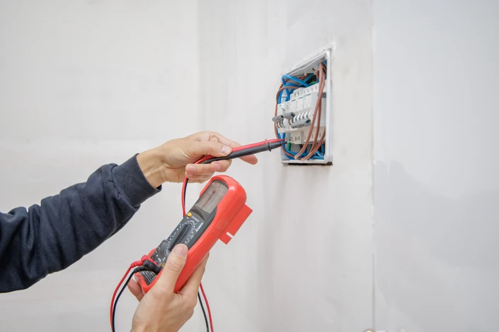 Un homme en t-shirt bleu applique de l'enduit ou de la peinture sur un mur intérieur blanc à l'aide d'une spatule