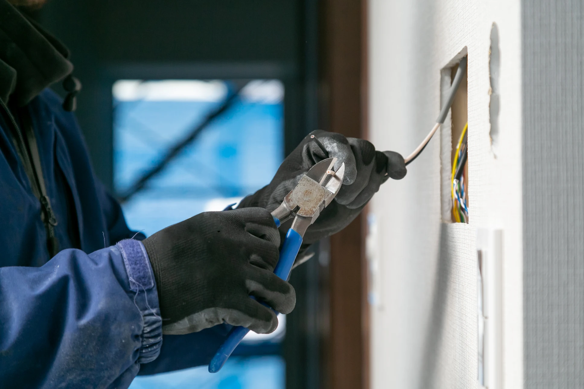 Un technicien intervient sur un tableau électrique domestique ouvert, utilisant un tournevis à manche isolé pour ajuster les disjoncteurs modulaires